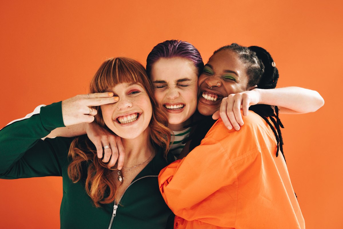 Drei Frauen umarmen sich vor einer orangefarbenen Wand