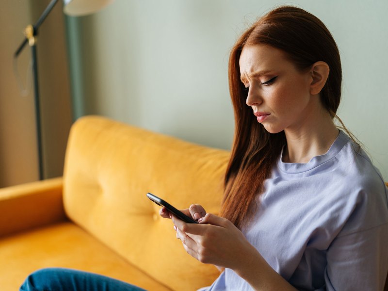 Frau sitzt auf einem gelben Sofa und blickt sorgenvoll