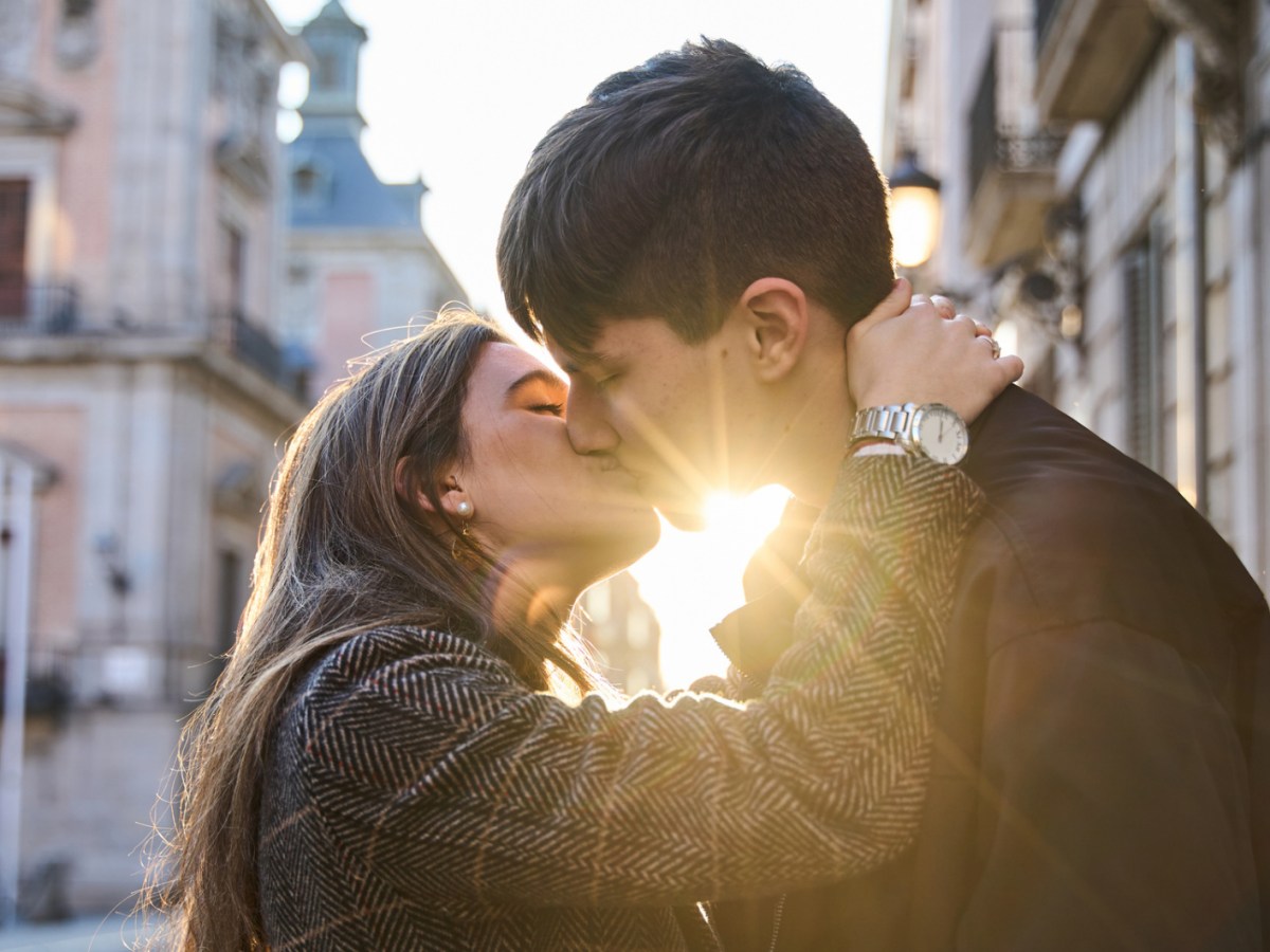 Mann und Frau, die sich auf einer Straße zwischen einem Sonnenstrahl küssen