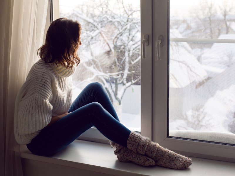 Frau sitzt vor Fenster, dahinter Winterlandschaft