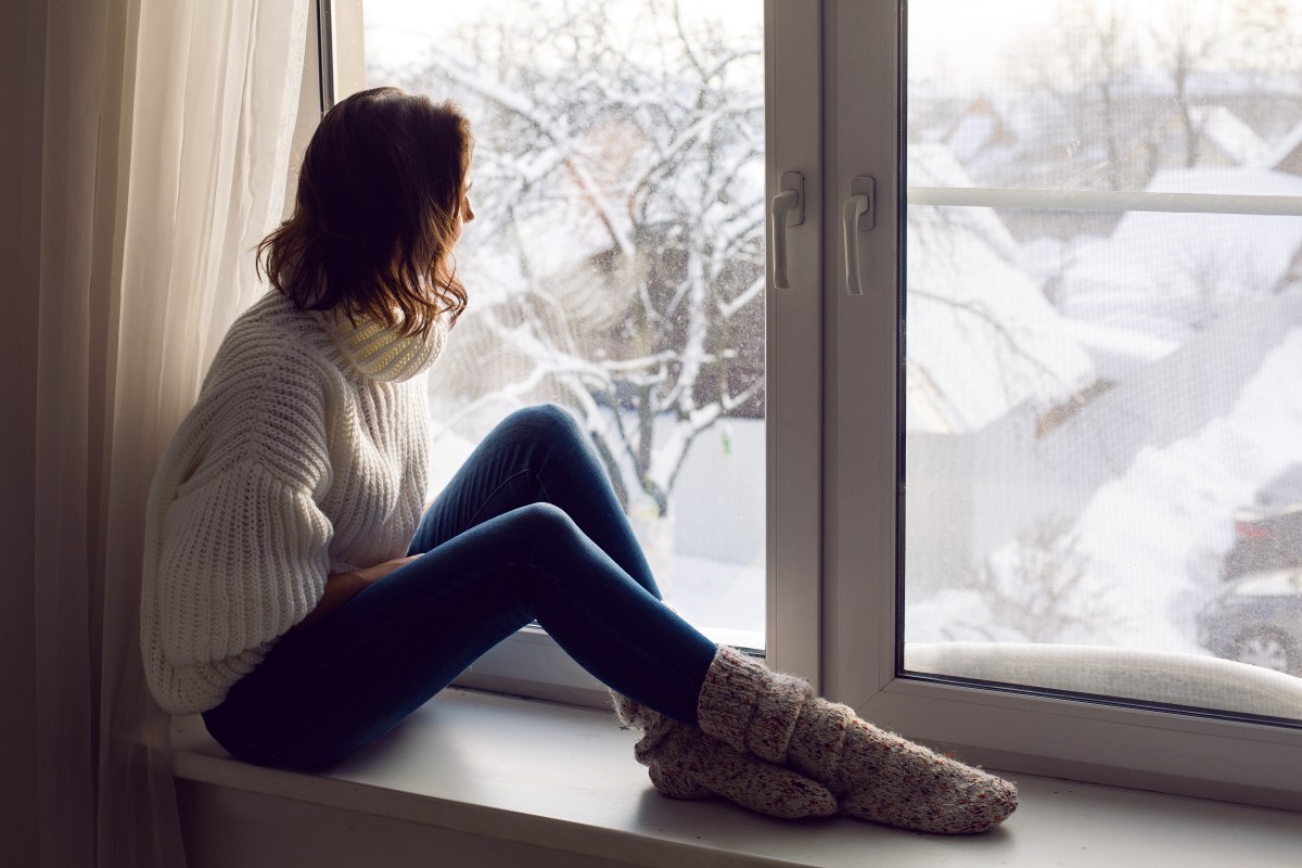 Frau sitzt vor Fenster, dahinter Winterlandschaft