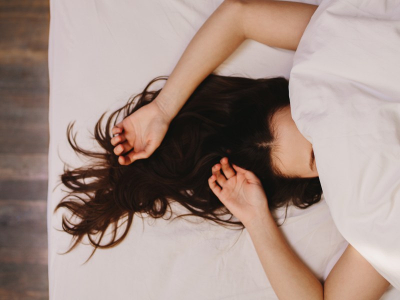 Frau im Bett, die ihre Arme über ihren Kopf streckt