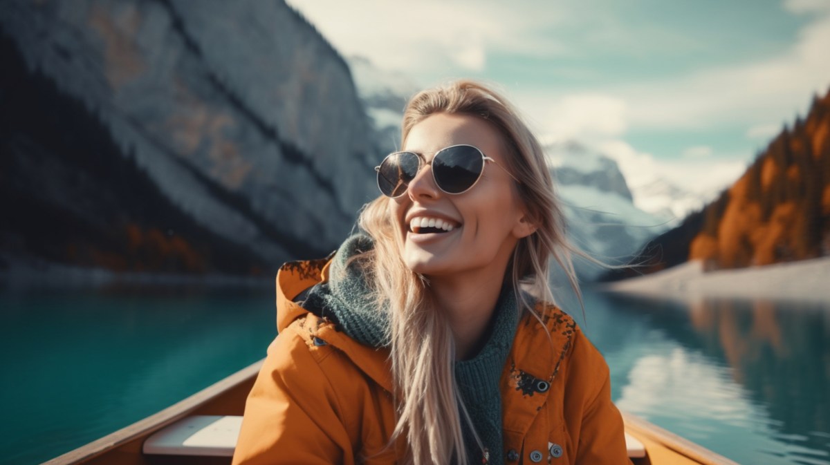 Frau auf einem Boot, die mit Sonnenbrille in die Ferne schaut, während im Hintergrund Berge zu sehen sind