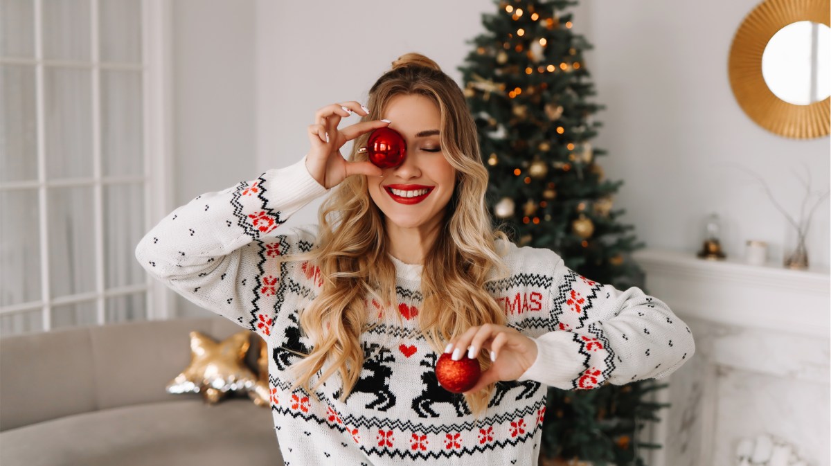 Frau mit Weihnachtspullover beim Schmücken des Baums.