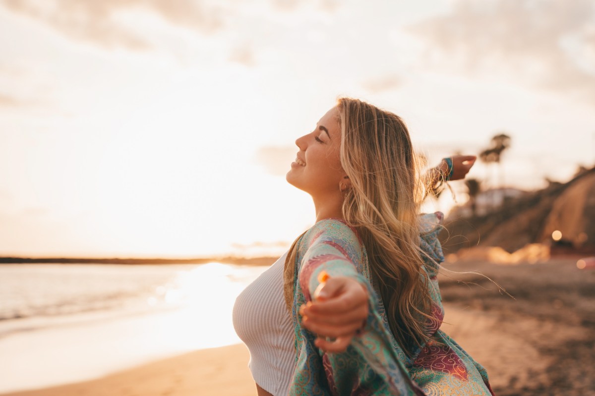 Eine Frau steht am Strand und breitet ihre Arme aus.