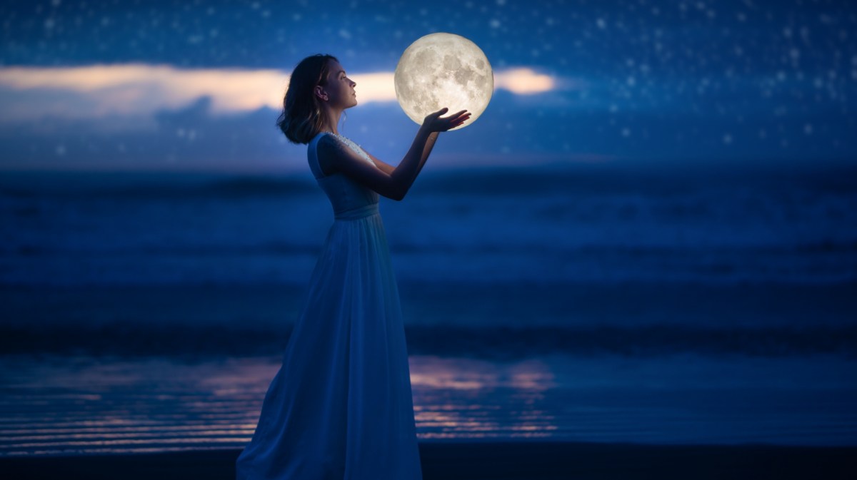 Frau in langem Kleid am Strand mit Mond in der Hand