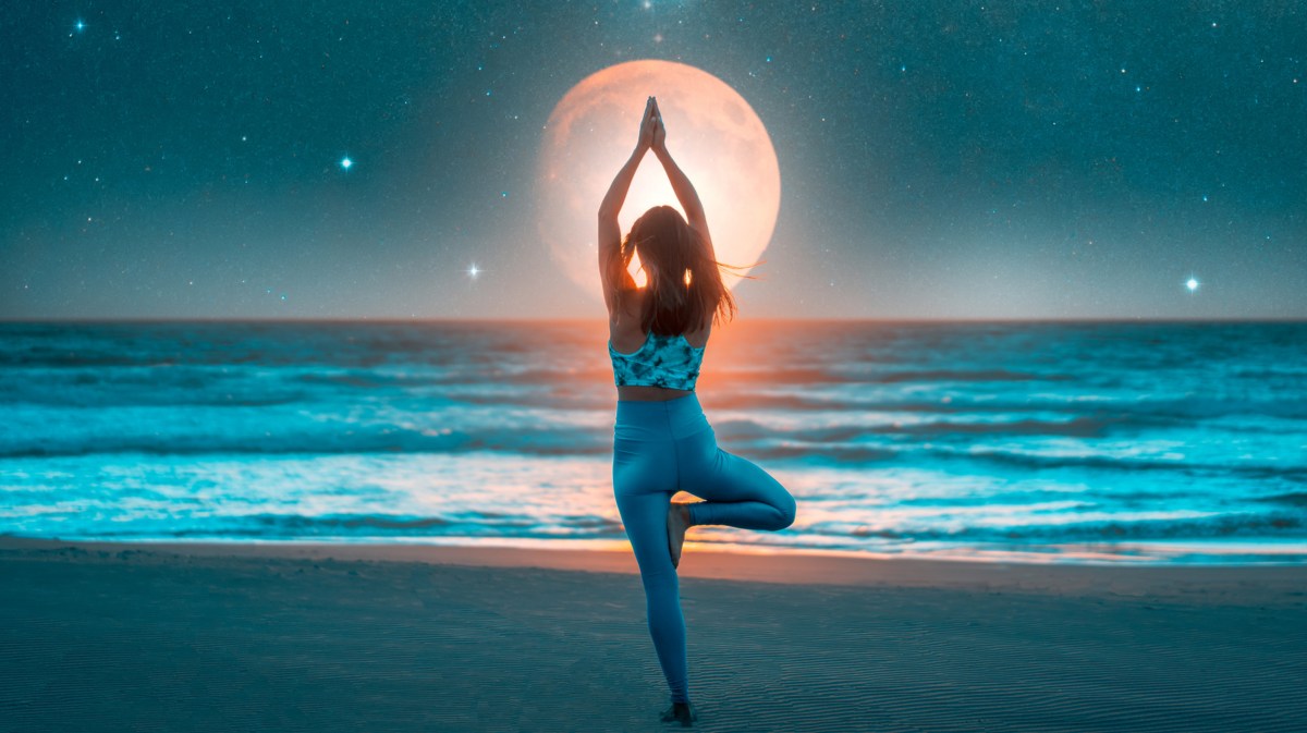 Frau macht Yoga-Übung am Strand, im Hintergrund ist der Mond