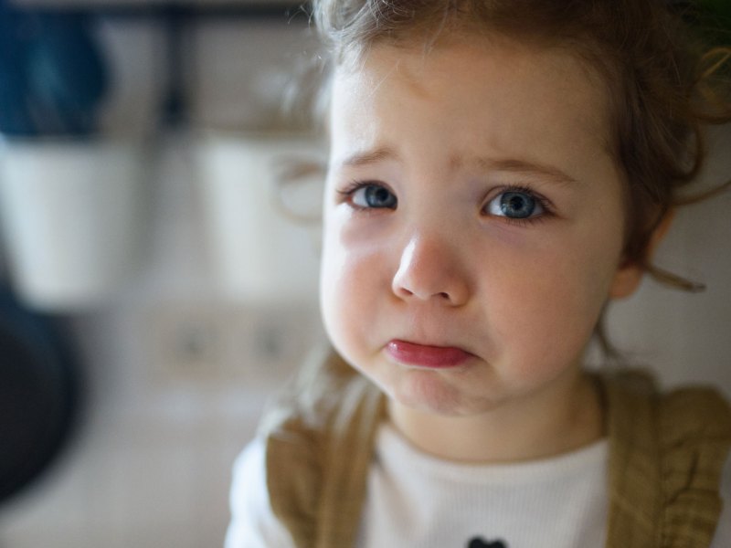 Kleines Mädchen, ca. 4 Jahre alt, schaut traurig und mit glasigen Augen in die Kamera.