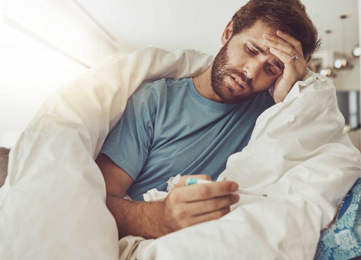 Thermometer, Stress und kranker Mann auf einem Sofa mit Kopfschmerzen, Fieber oder Grippe männliche Person mit Schwindel, Risiko oder Angst vor einer Covid-Infektion im Wohnzimmer