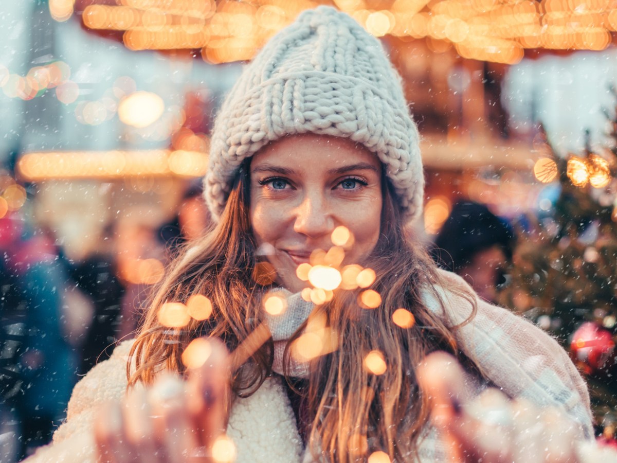 Frau mit Mütze auf dem Weihnachtsmarkt mit Wunderkerze in der Hand