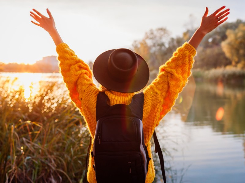 Frau mit Hut und Rucksack an einem See im Herbst bei Sonnenuntergang