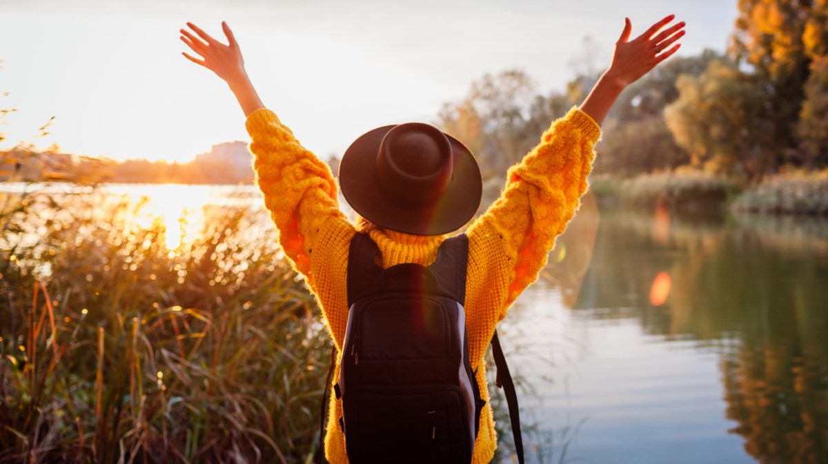 Frau mit Hut und Rucksack an einem See im Herbst bei Sonnenuntergang