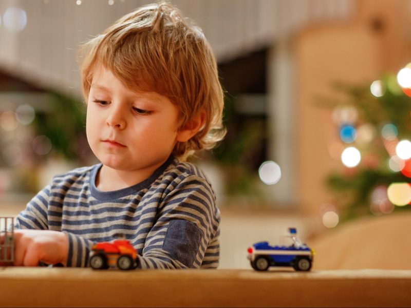 Blonder Junge spielt mit Spielzeugautos vor Weihnachtsbaum