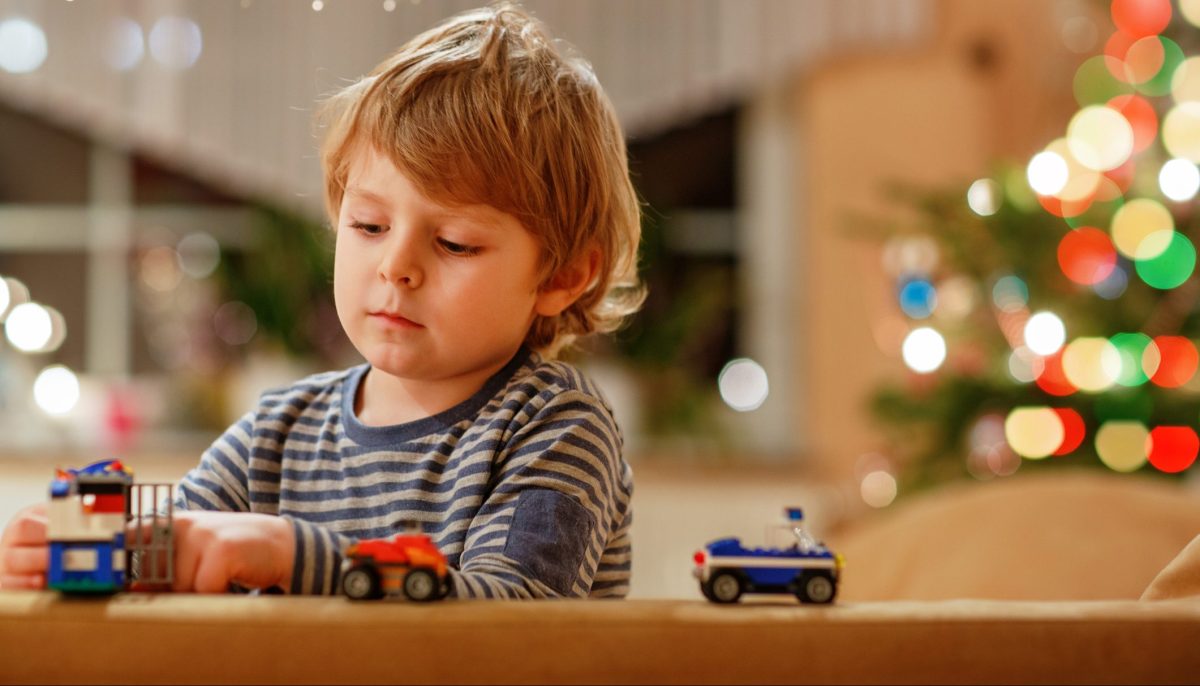 Blonder Junge spielt mit Spielzeugautos vor Weihnachtsbaum