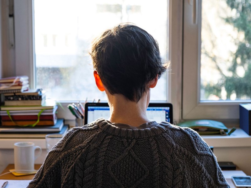 Eine Frau sitzt am Schreibtisch und schaut aus dem Fenster.