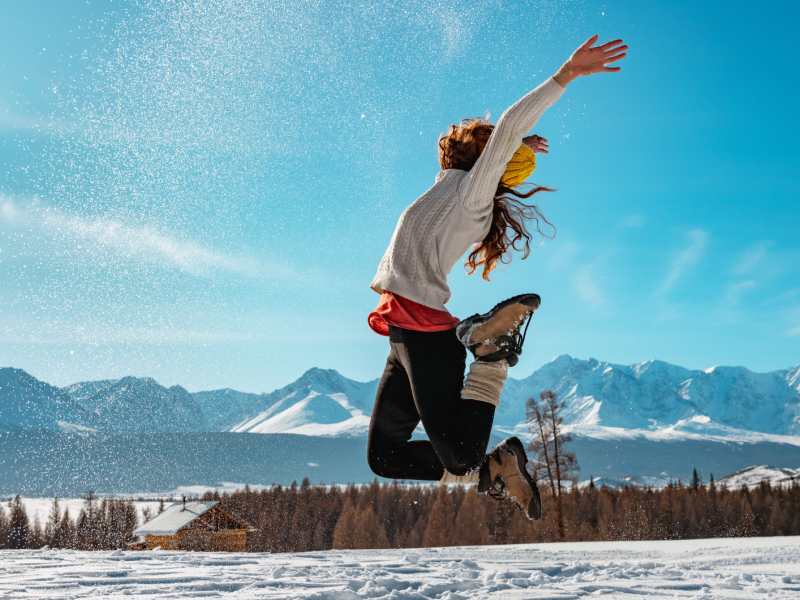 Frau die im Schnee in die Luft springt und die Arme hochreißt