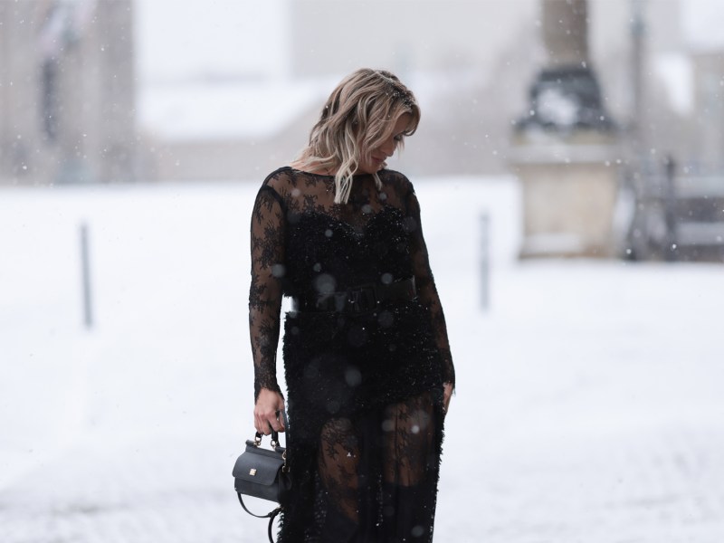 Frau mit schwarzem Kleid beim Winterspaziergang durch den Schnee.