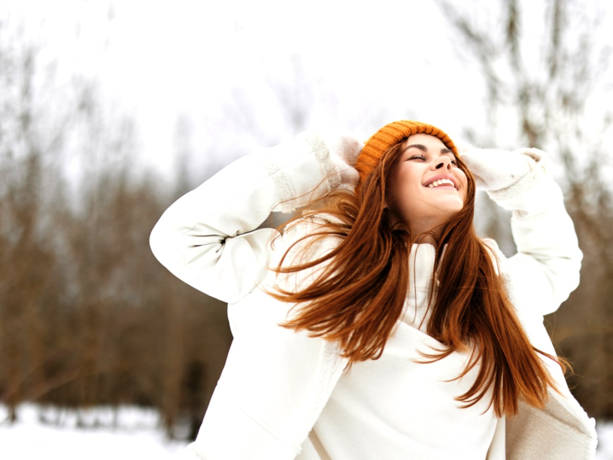 Frau im Schnee mit roten Haaren die lacht und sich an den Kopf packt
