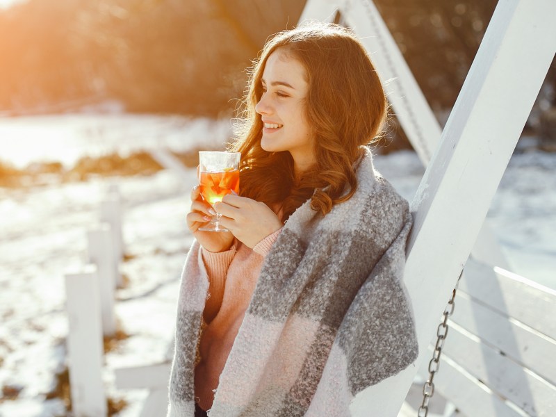 Frau vor Schneelandschaft, die lächelt und ein Getränk in der Hand hält