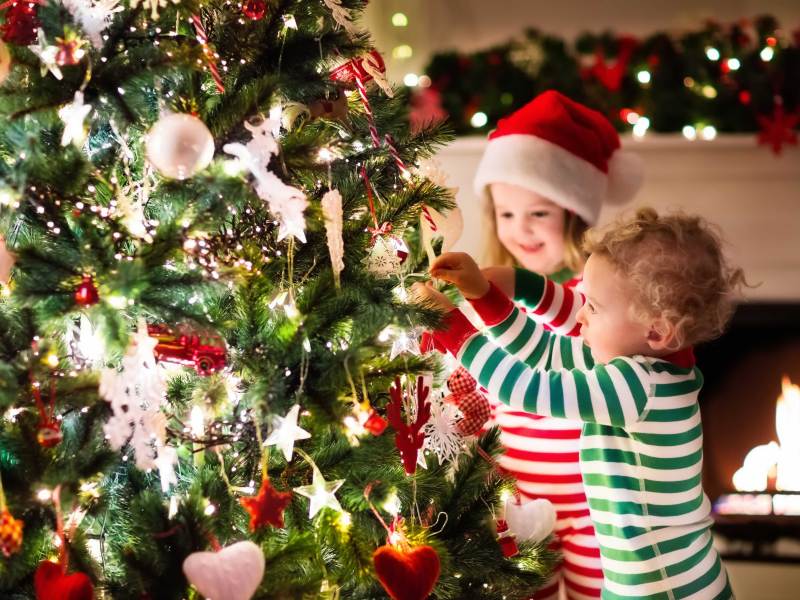 Zwei kleine Kinder schmücken in Schlafanzügen den Weihnachtsbaum.