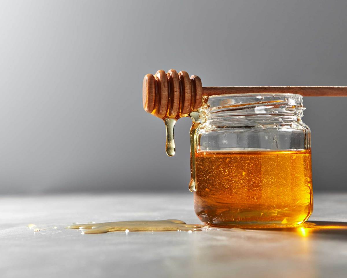 Tropfen von natürlichem frischen Honig aus Glas auf einem grauen Küchentisch.