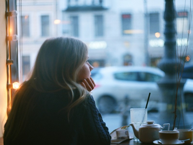 Frau in einem Café am Fenster, die nachdenklich hinausschaut
