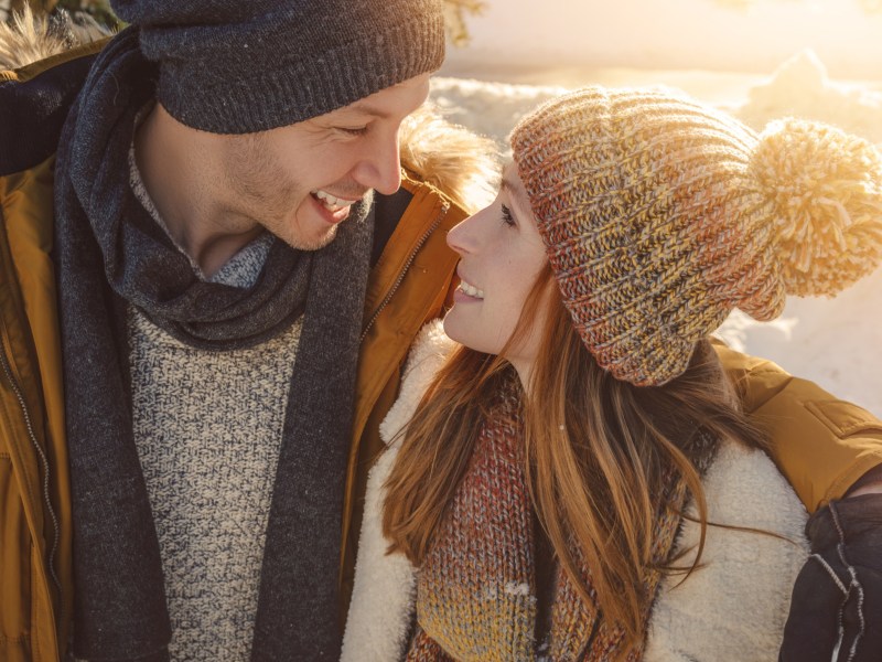 Verliebtes Paar im Schnee mit Winterkleidung schaut sich in die Augen