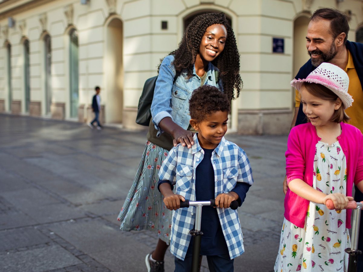 Stieffamilie ist in der Stadt unterwegs. Die beiden Kinder fahren mit Rollern.