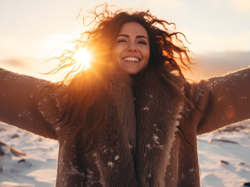 Fröhliche Frau mit Locken und Mantel bei Sonnenuntergang