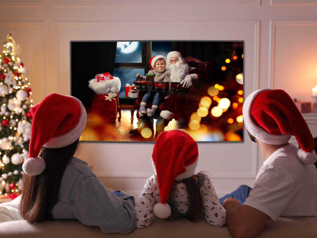 Mutter, Vater und Tochter sitzen in ihrem weihnachtlichen Wohnzimmer vorm TV und schauen einen Weihnachtsfilm.