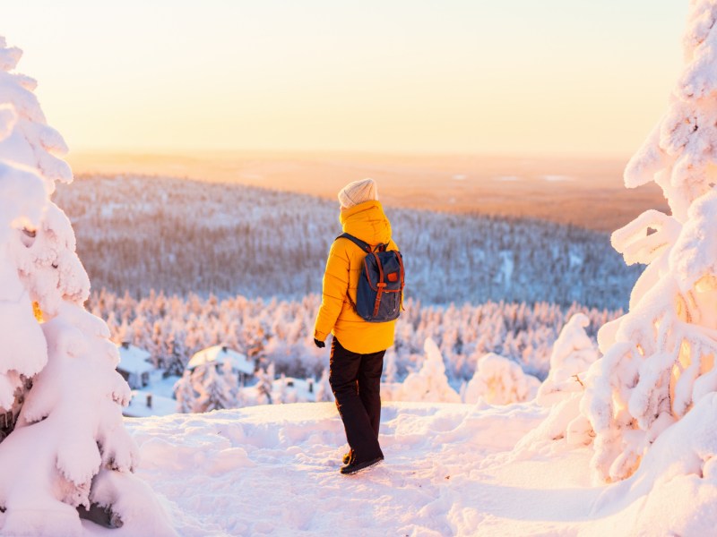 Person in gelber Winterjacke steht in verschneiter Landschaft