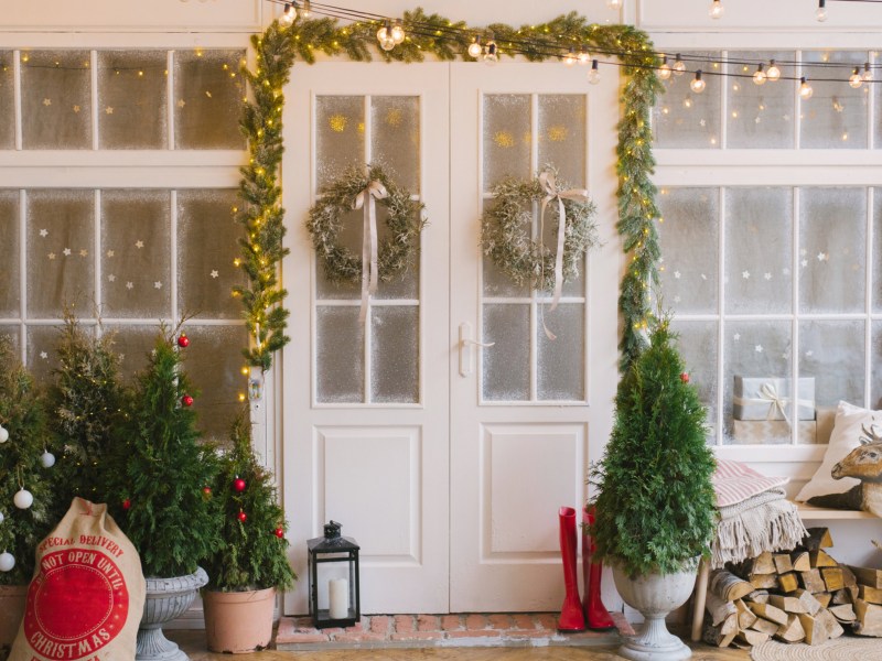 Tür, die weihnachtlich geschmückt ist, mit Girlande und grünen Tannenzweigen.