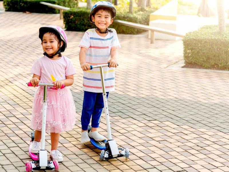Zwei kleine Kinder, ca. 4 und 6 Jahre, fahren draußen alleine mit ihren Rollern herum.
