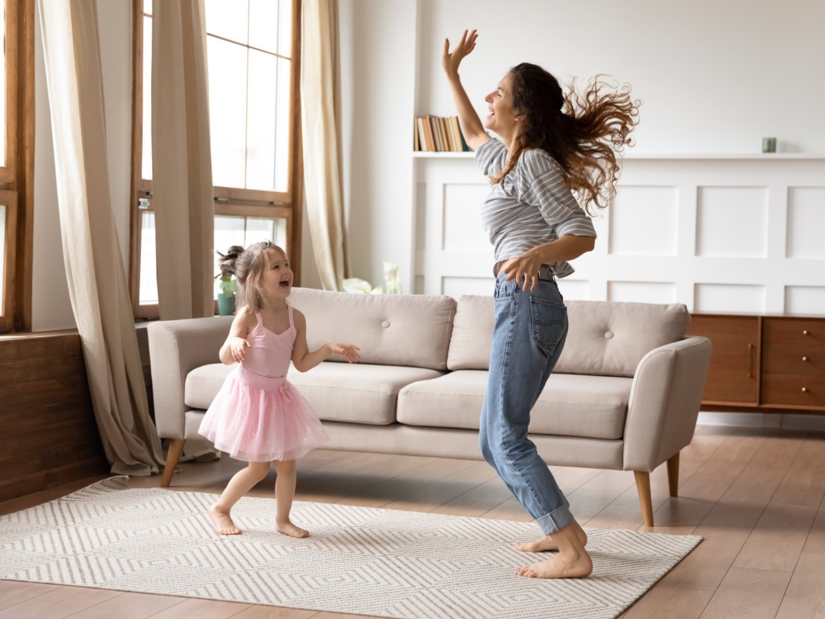 Eine Frau tanzt mit ihrem Kind im Wohnzimmer.