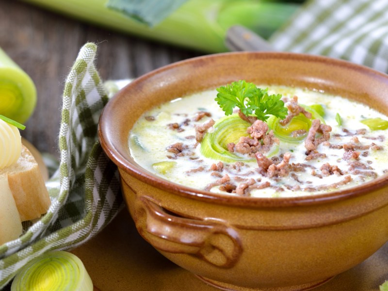 Käse-Lauch-Suppe mit Hackfleisch in braunem Keramiktopf.