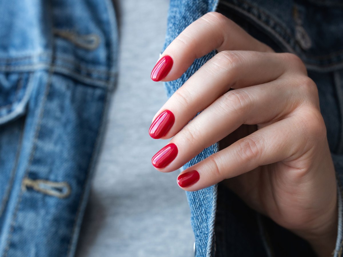 Frau mit perfekten roten Nägeln, die statt Nagellack Nagelfolien verwendet.
