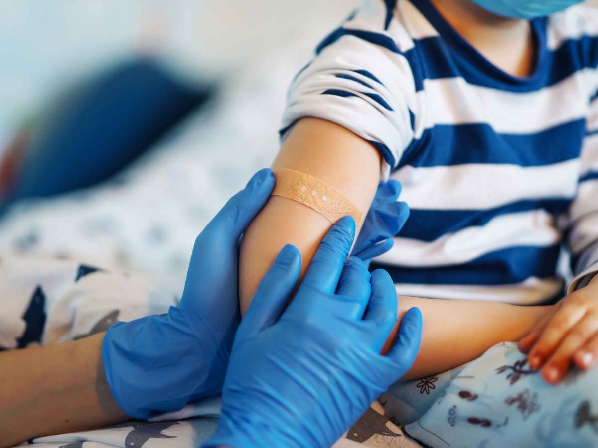 Nahaufnahme eines Kinderarms nach einer Impfung. Der Arzt oder die Ärztin klebt gerade das Pflaster auf die Einstichstelle.