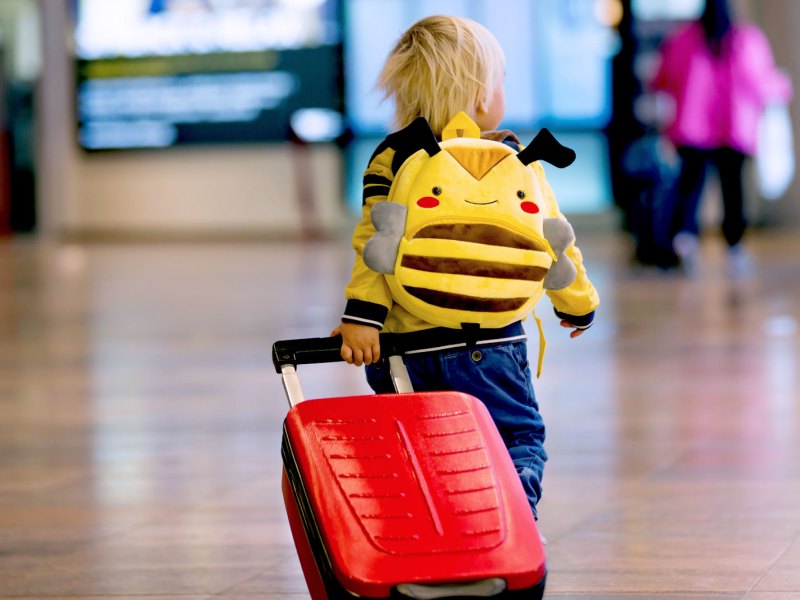Kleines Kind, ca. vier Jahre, mit Rucksack und Rollkoffer am Flughafen.