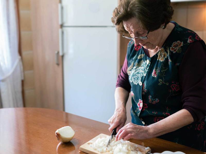 Omas Hausmittel gegen Husten: Ältere Frau schneidet Zwiebel auf Brett