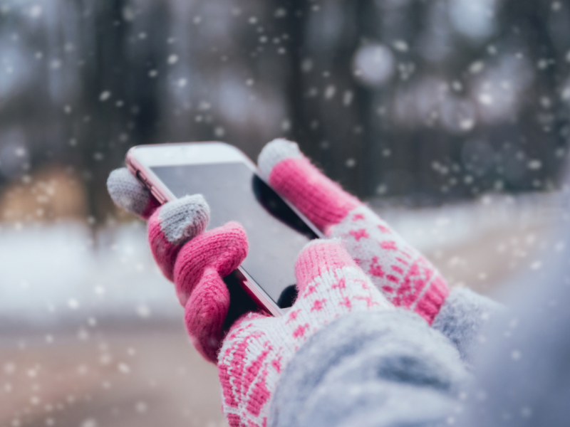 Zwei Hände mit Handschuhe halten ein Smartphone draußen im Schnee