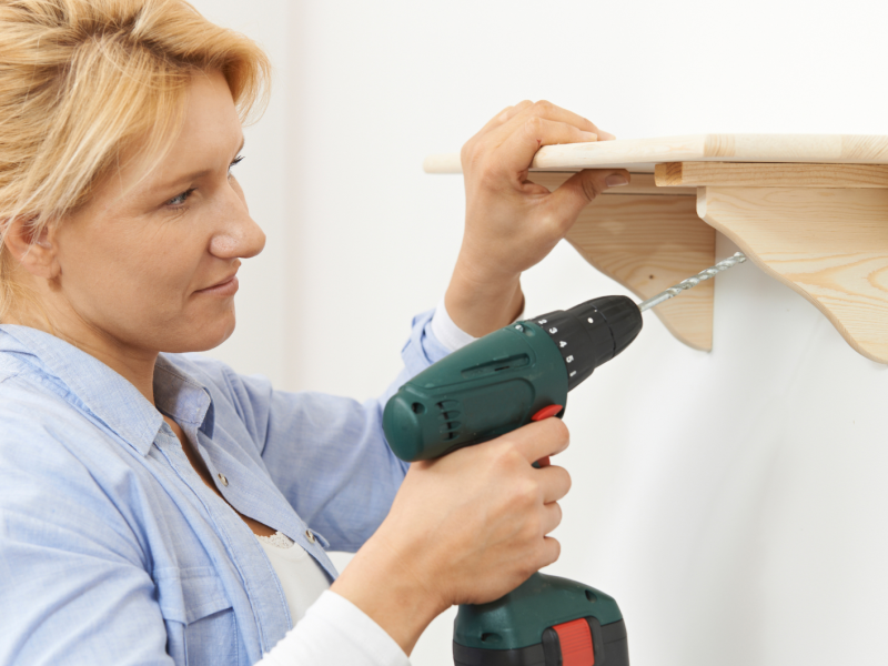 Frau bohrt Regal an die Wand