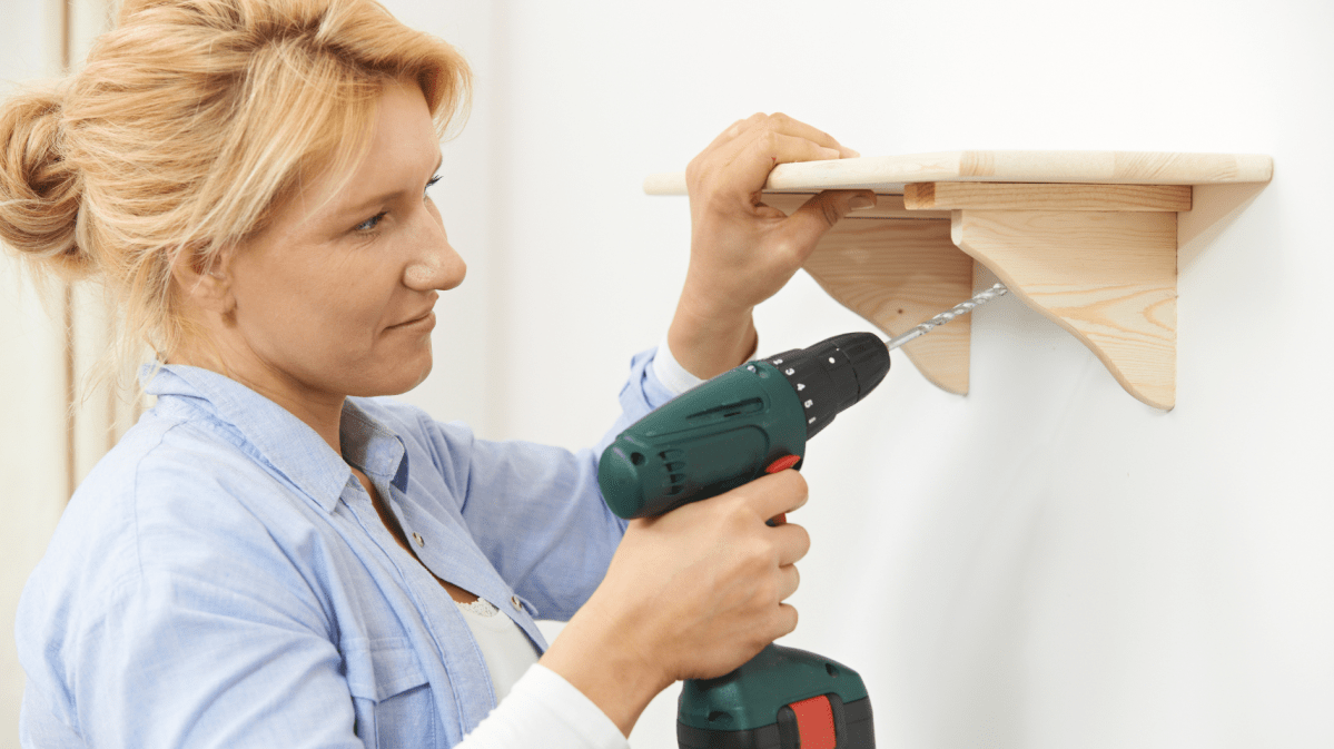 Frau bohrt Regal an die Wand