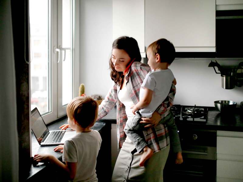 Beschäftigte Mutter von zwei Jungs arbeitet am Laptop.