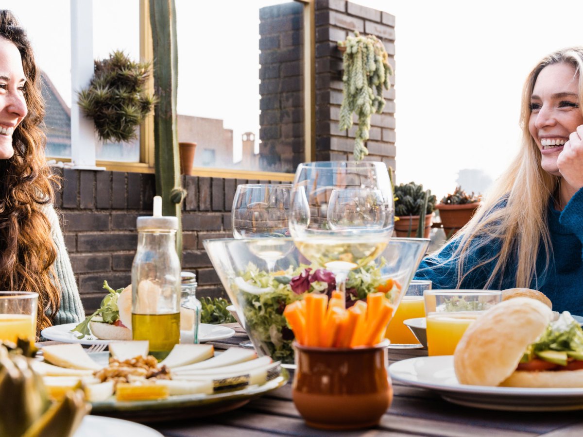 Frauen lachend am Tisch mit vielen gesunden Speisen & Getränken