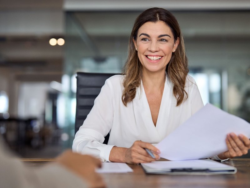 Erfolgreiche Business Frau in weißer Bluse sitzt lächelnd an Konferenztisch