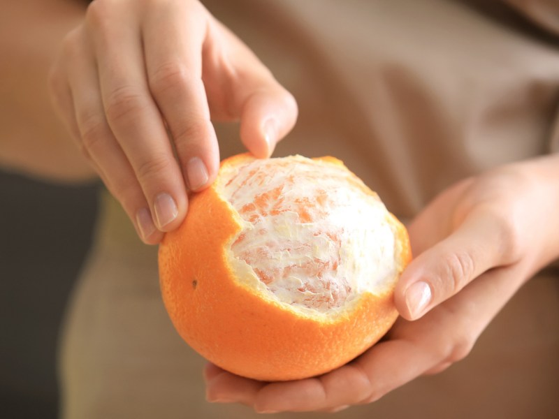 Eine Frau schält eine Orange.