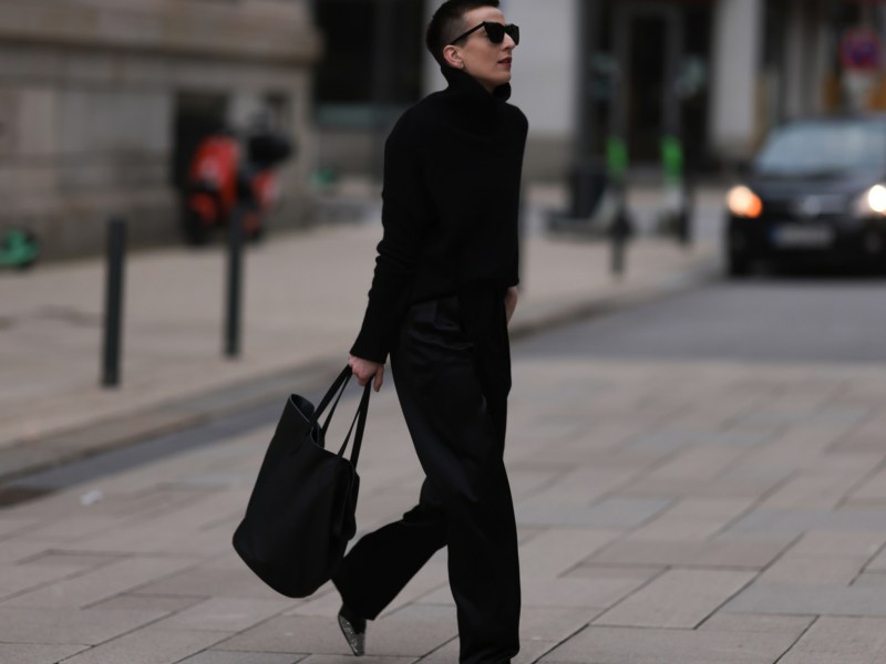 Frau ganz in schwarz gekleidet, street style, hält schwarzen Shopper in Hand.