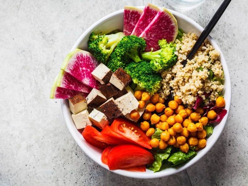 Buddha-Schale mit Quinoa, gebratenen Kichererbsen, geräuchertem Tofu und Gemüse in weißem Teller, Ansicht von oben.