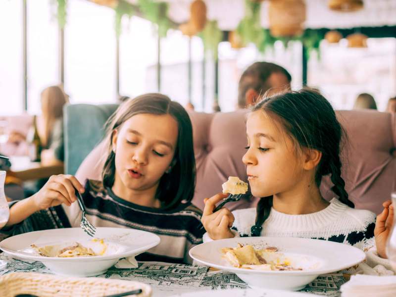 Zwei Mädchen, ca 9 Jahre alt, sitzen im Restaurant und essen Nudeln.