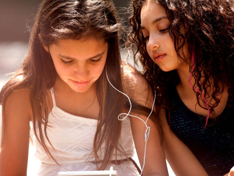 Zwei Mädchen sitzen am Tablet und hören Musik.